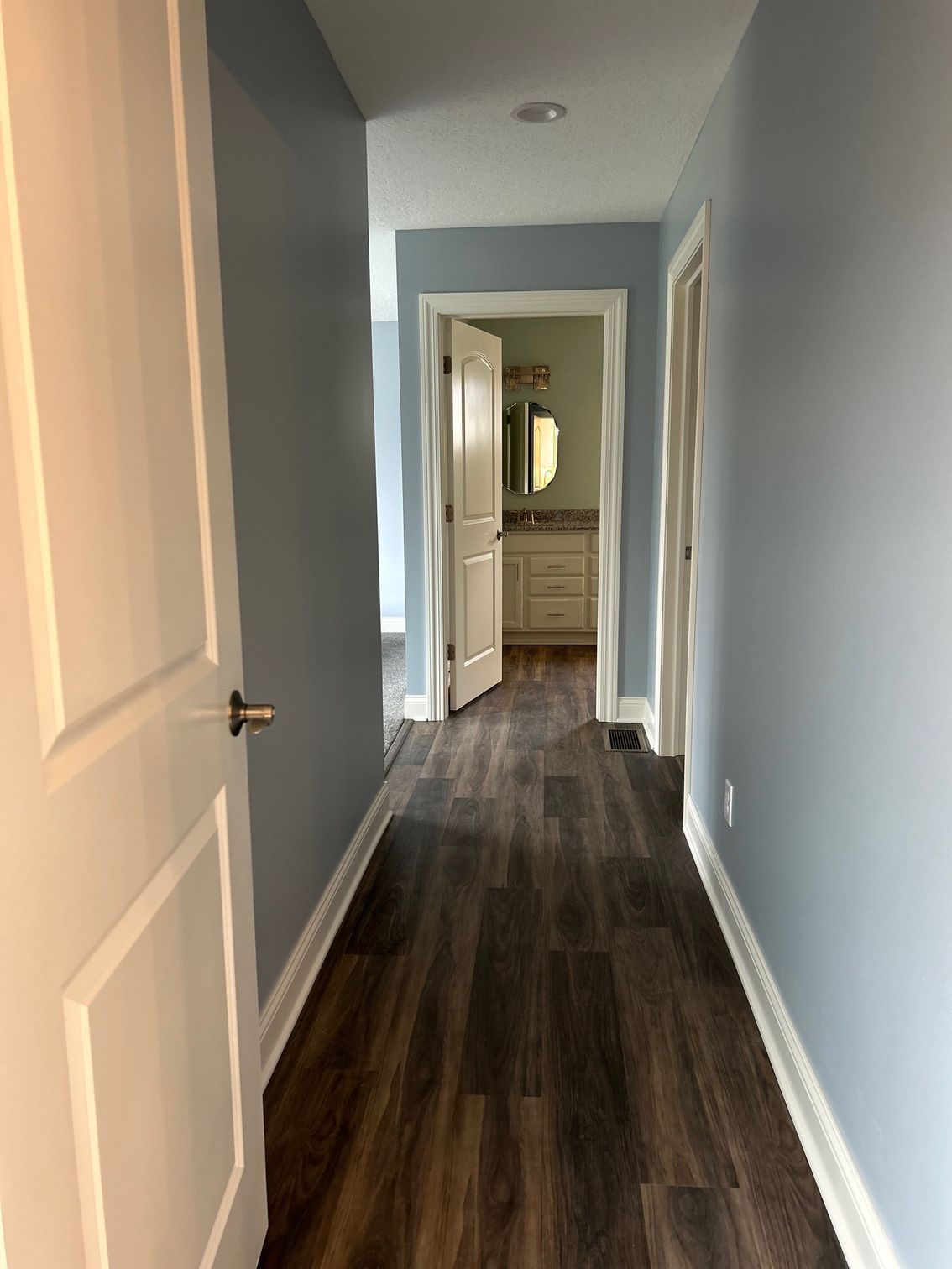 A hallway with hardwood floors and blue walls leading to a bathroom.