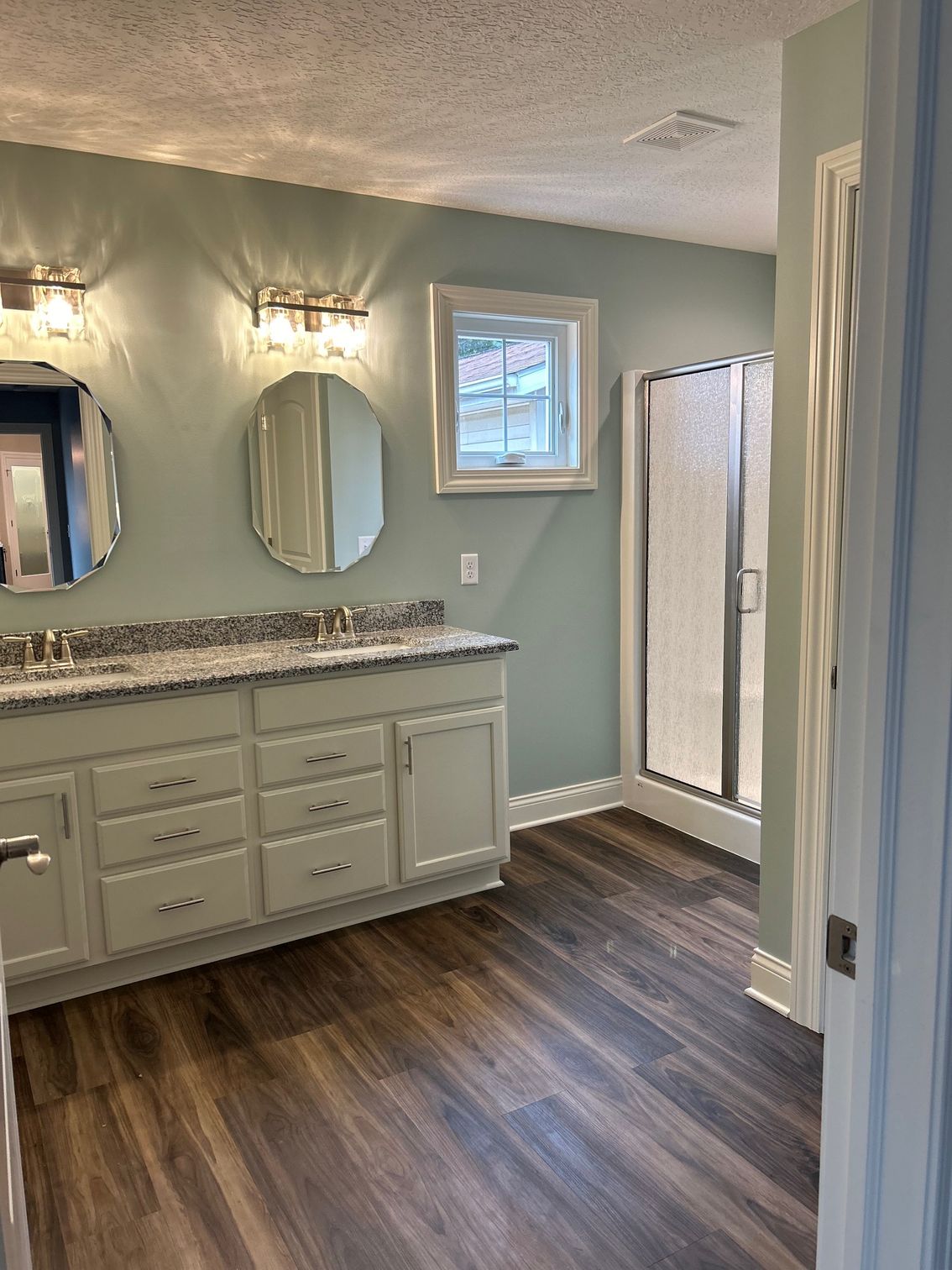 A bathroom with two sinks , two mirrors and a walk in shower.