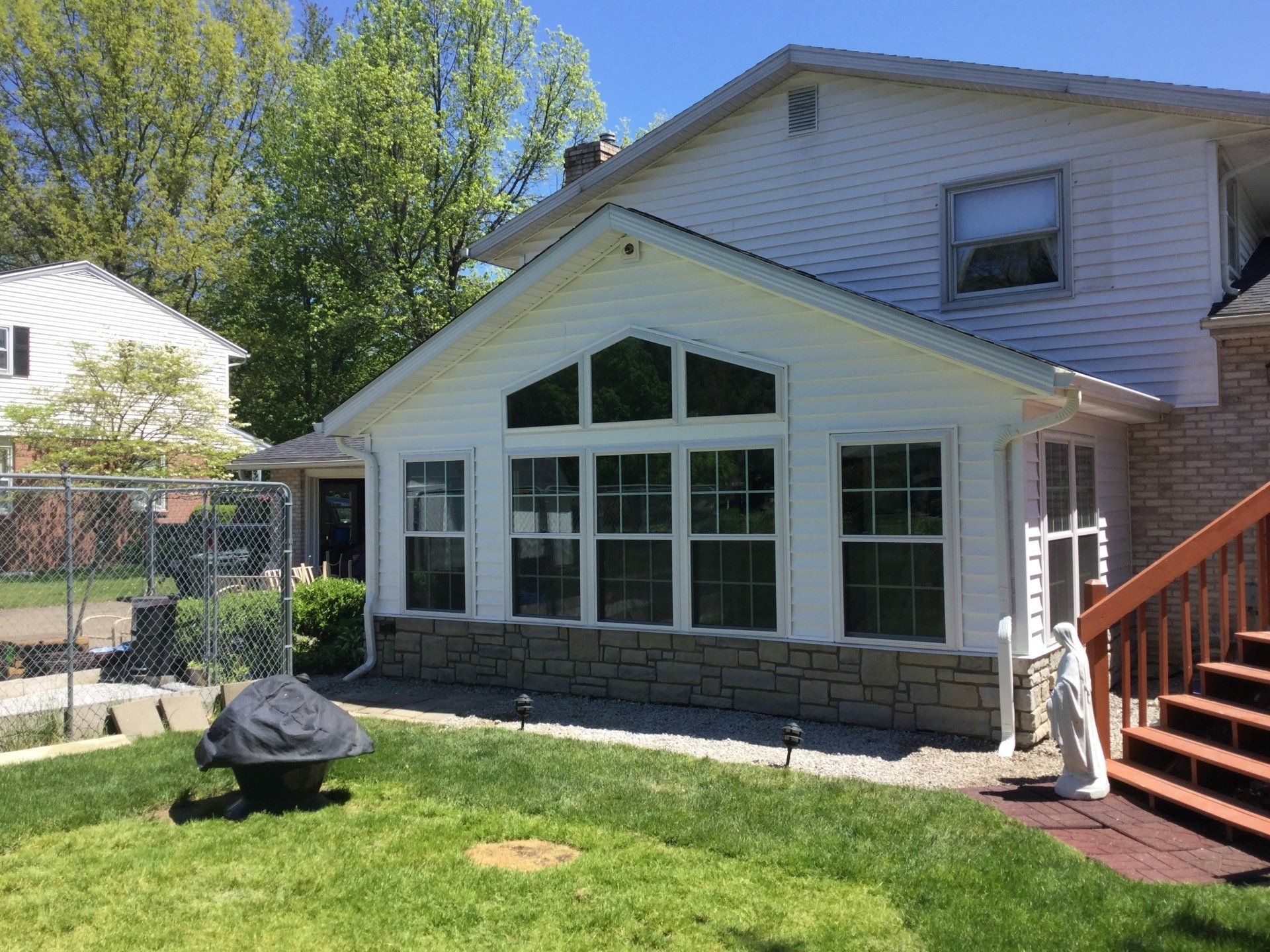 A white house with a sunroom and stairs in the backyard.