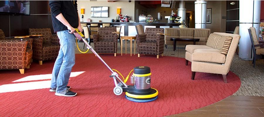 A man is using a vacuum cleaner to clean a red carpet in a living room.