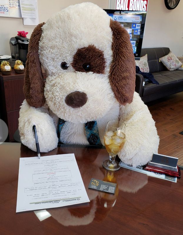 A stuffed dog is sitting at a desk with a glass of wine