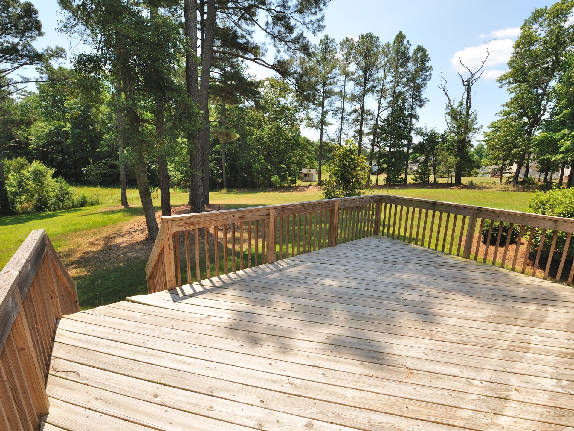 Wooden deck overlooking a grassy yard and trees under a sunny sky.
