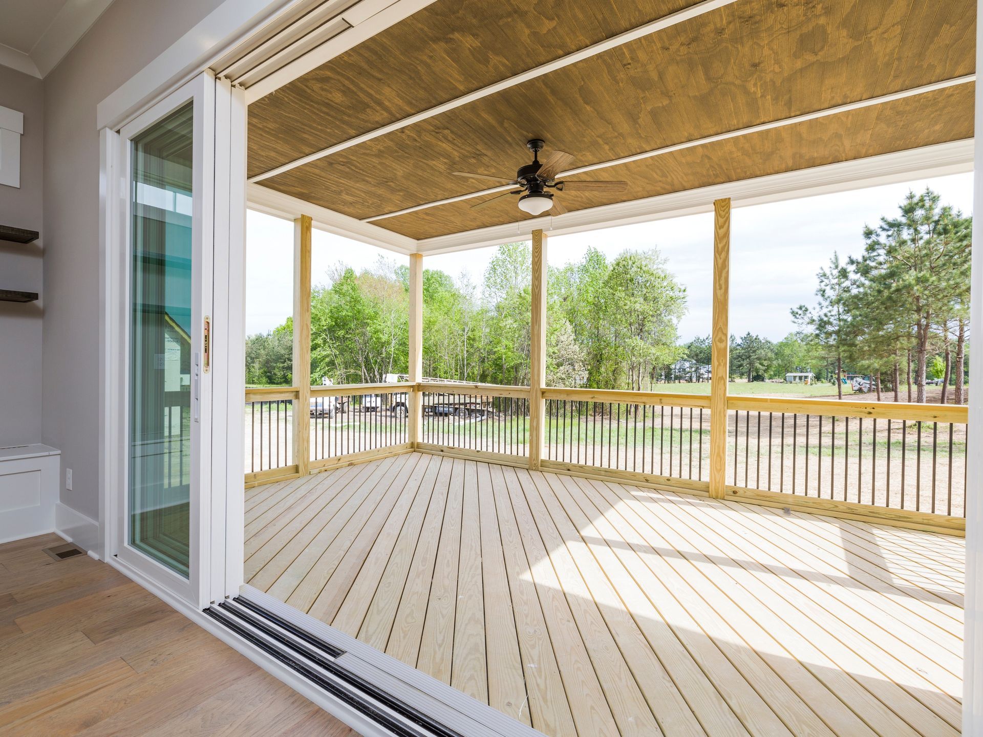 Light wood deck with screened porch, sliding glass door open to view of trees.