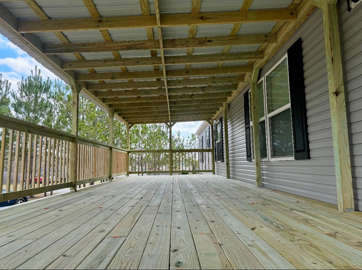 Wooden porch with a light-colored roof extending from a lilac-sided house with black shutters.