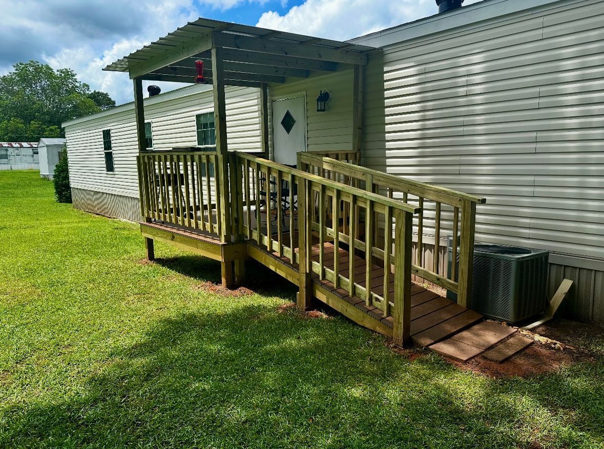 Mobile home with wooden ramp and porch, on green lawn.