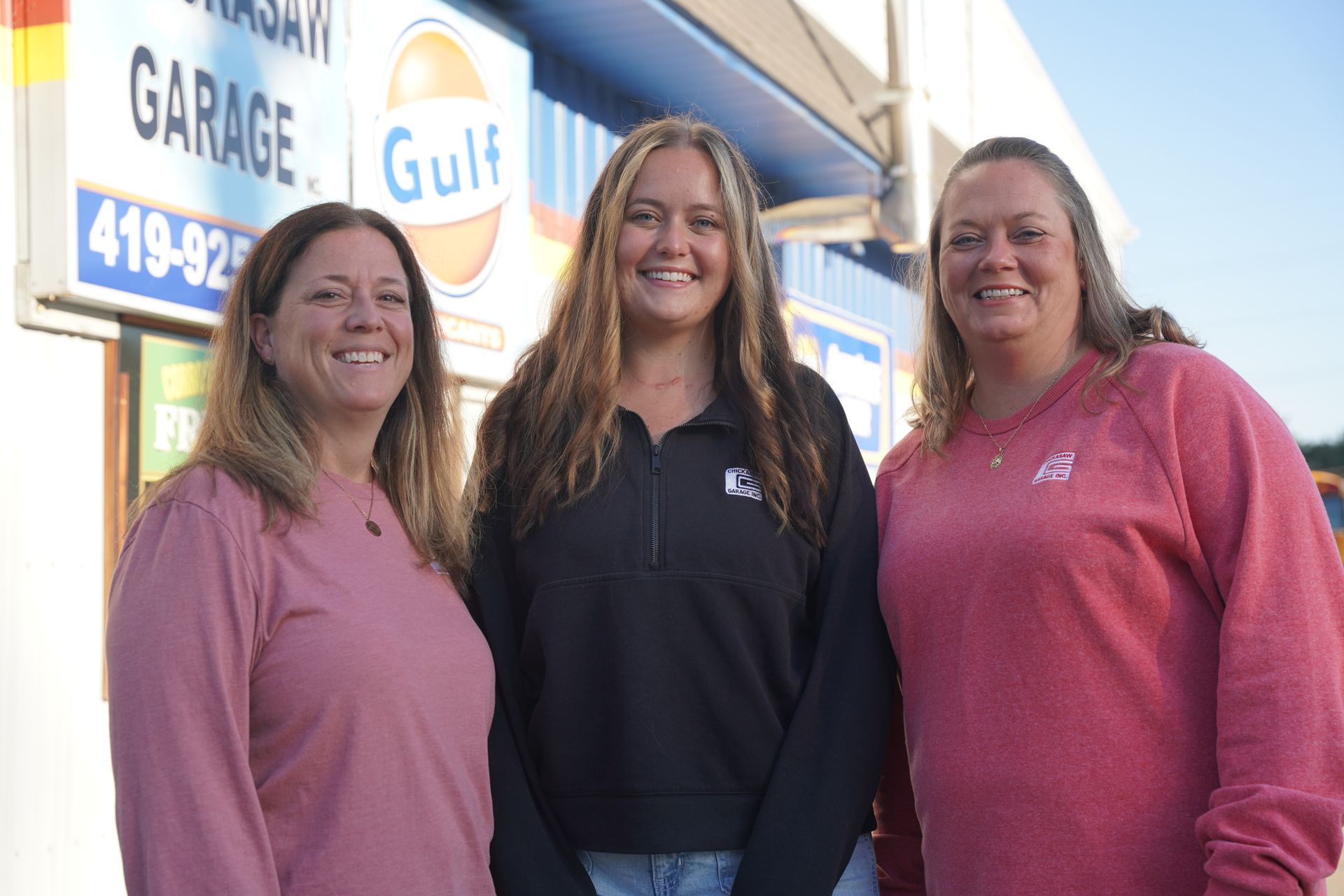 Three women stand outside a garage with a