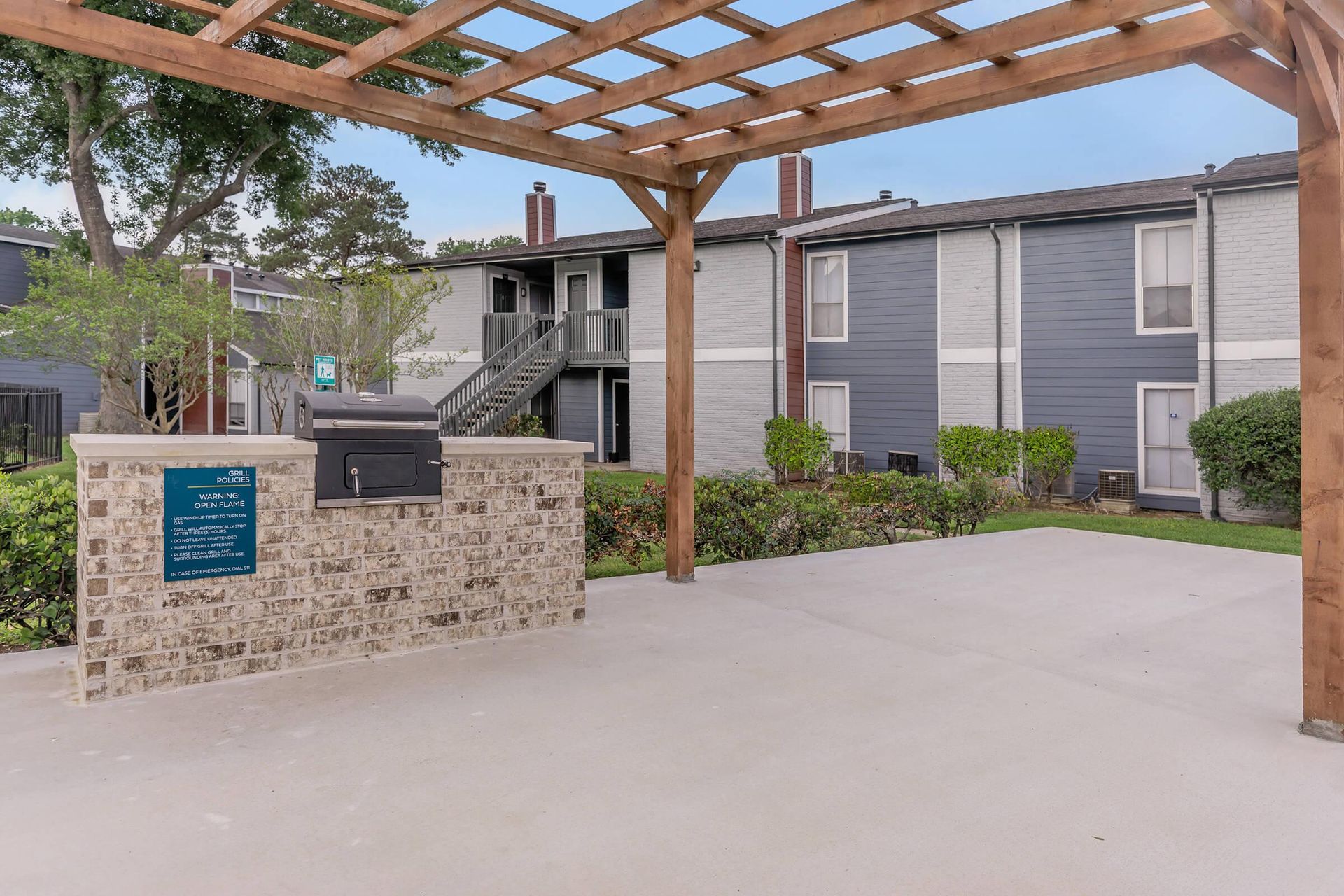 There is a grill under a pergola in front of a building at Serena Apartment Homes.