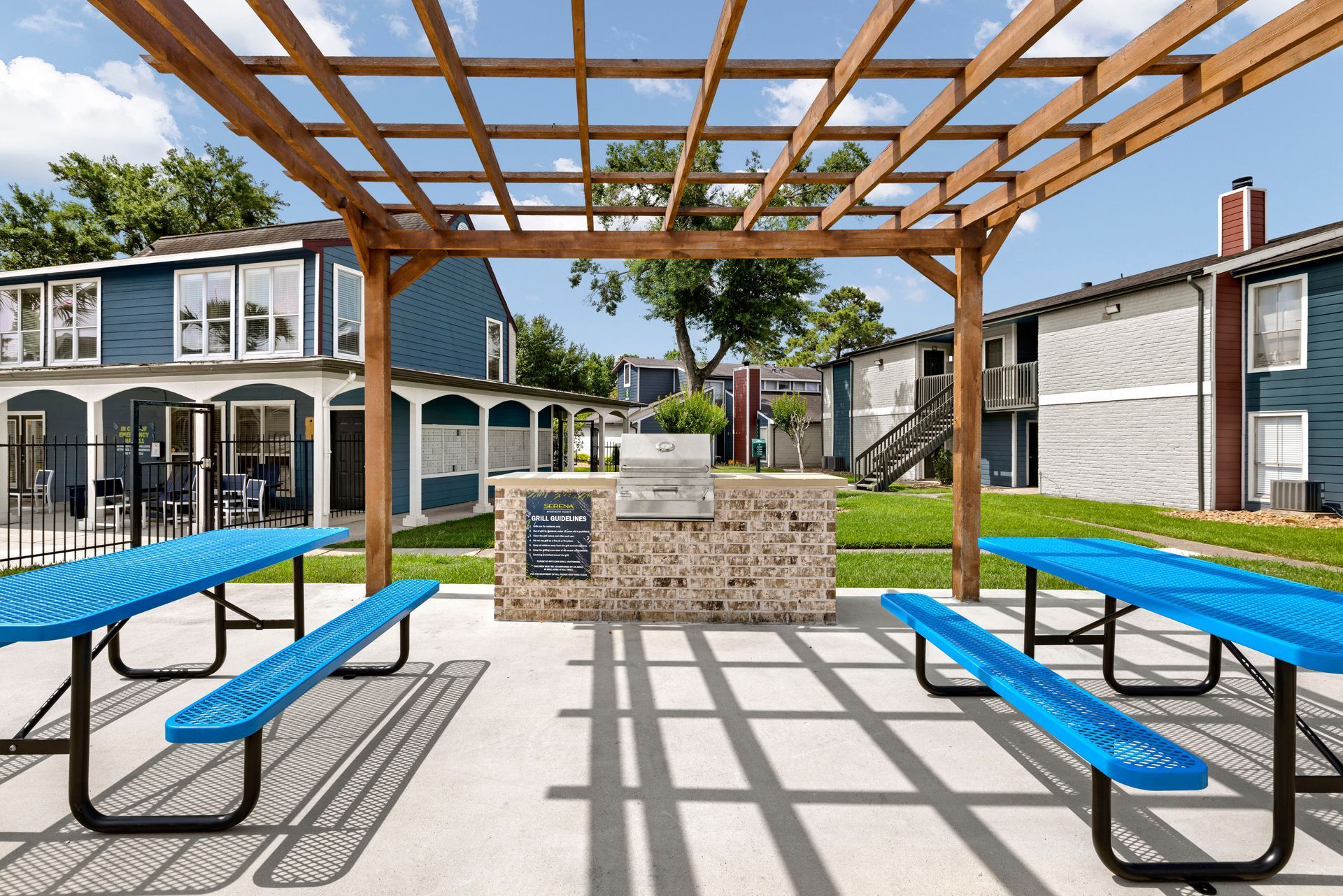 There is a grill under a pergola in front of a building at Serena Apartment Homes.