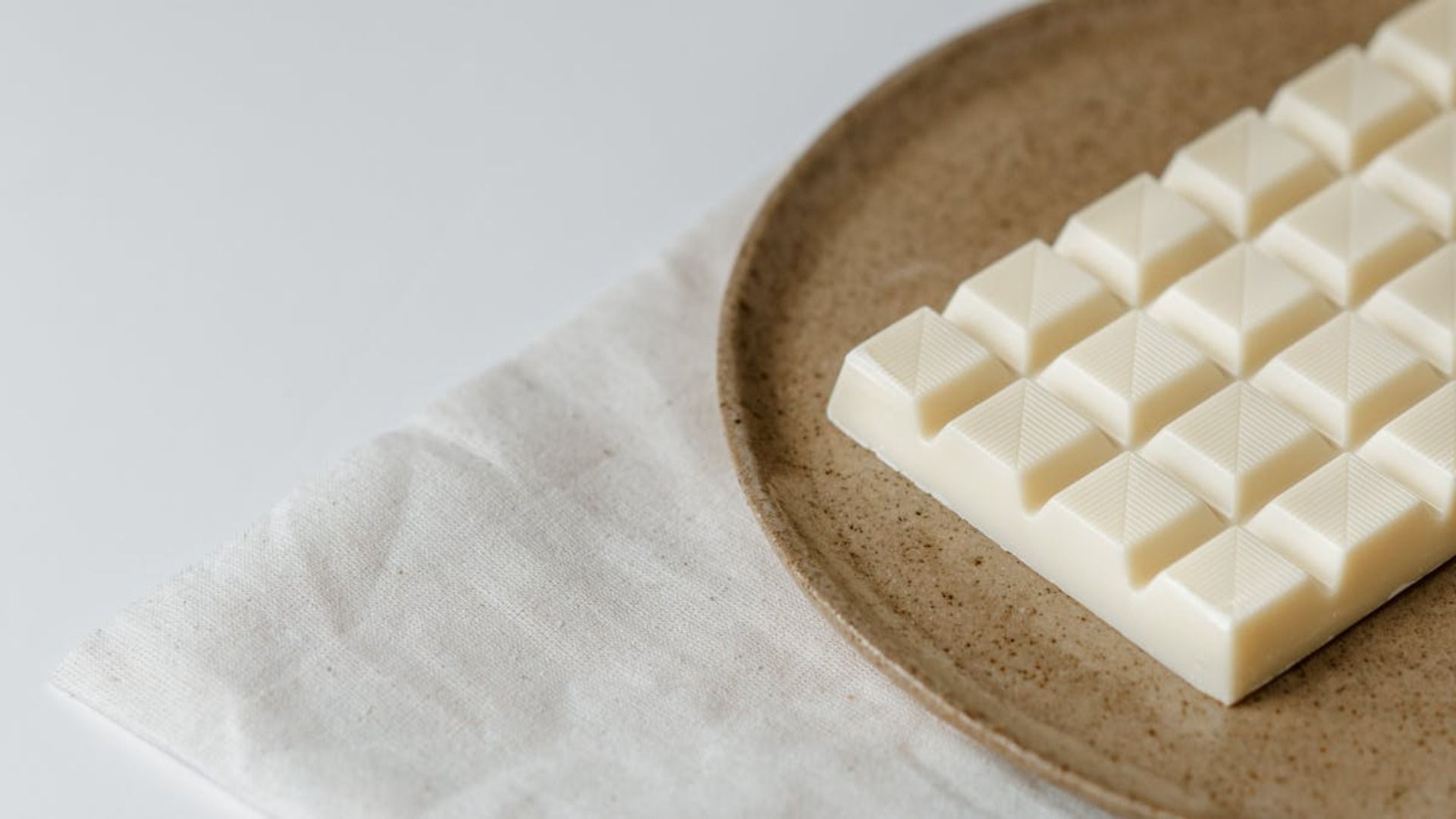 Barra de chocolate blanco sobre un plato marrón moteado, que reposa sobre un paño blanco.