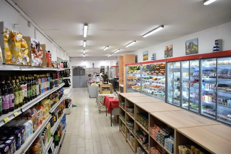 Un corridoio di un supermercato ben illuminato, con scaffali pieni di prodotti alimentari e un lungo banco frigo sulla destra.