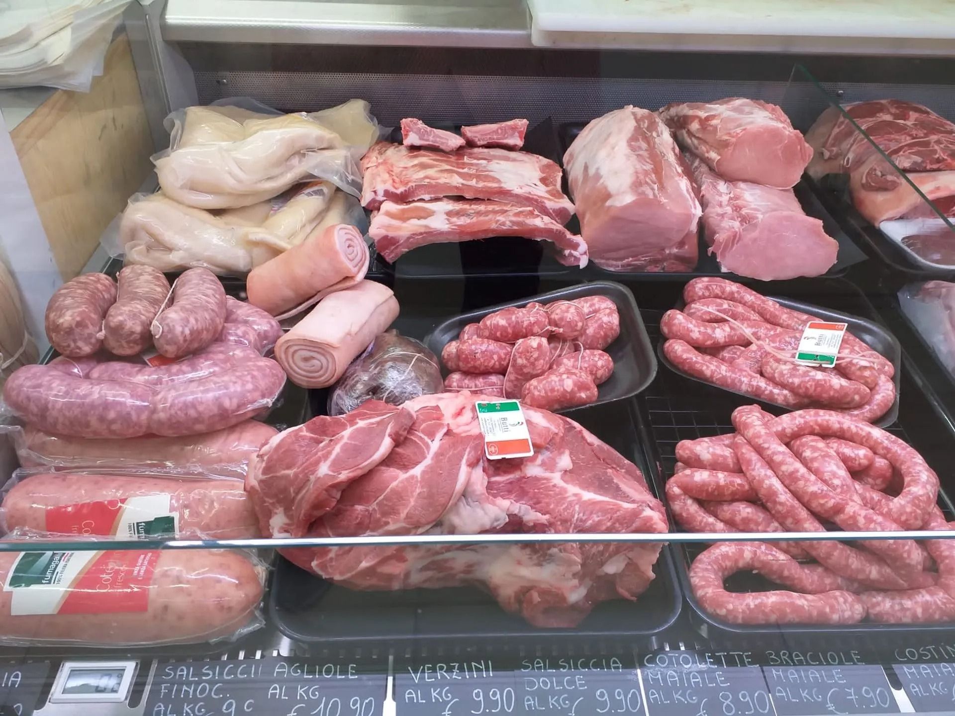 Una vetrina refrigerata di una macelleria, piena di vari tagli di carne di maiale cruda, salsicce e salumi affettati.