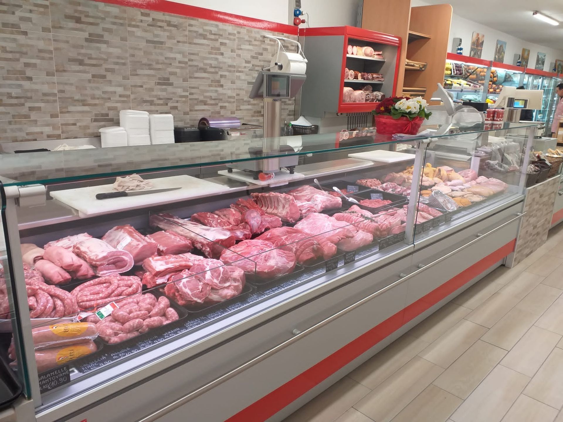 Una vetrina refrigerata all'interno di una macelleria, piena di vari tagli di carne cruda e salsicce.
