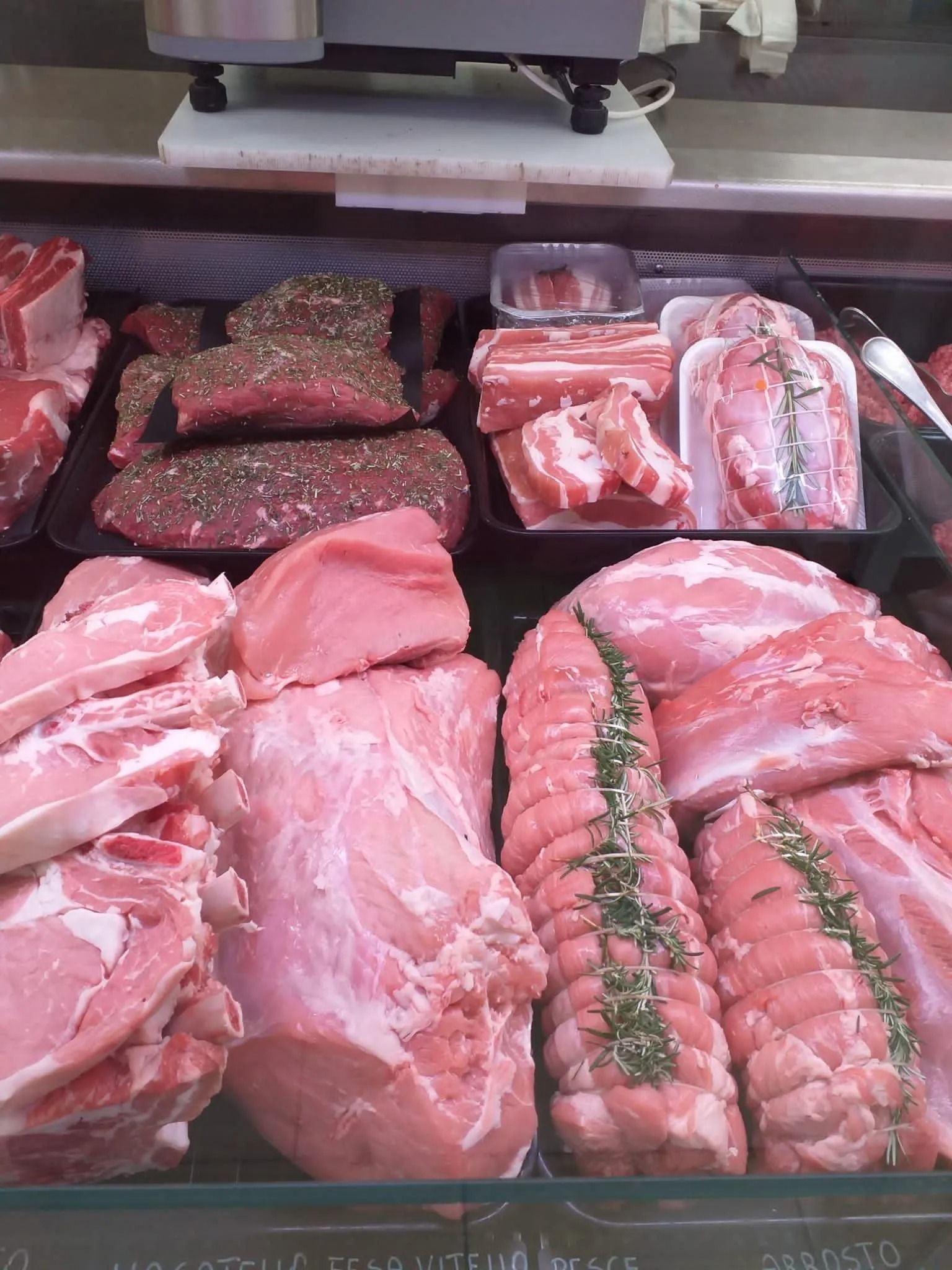 Una vetrina refrigerata di salumi e formaggi, piena di vari tagli di carne cruda, tra cui bistecche condite e arrosti di maiale.