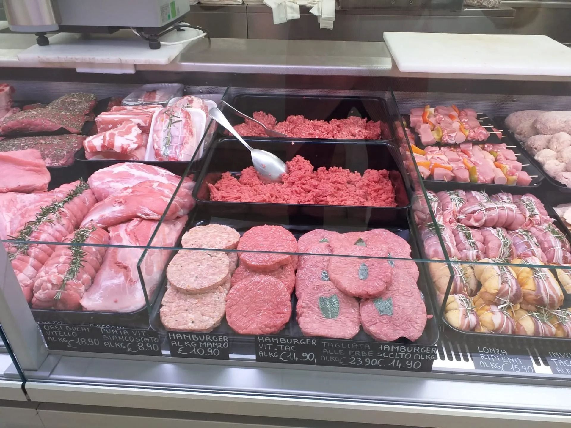 Una vetrina refrigerata in una macelleria, piena di vari tagli di carne cruda, carne macinata e hamburger già pronti.