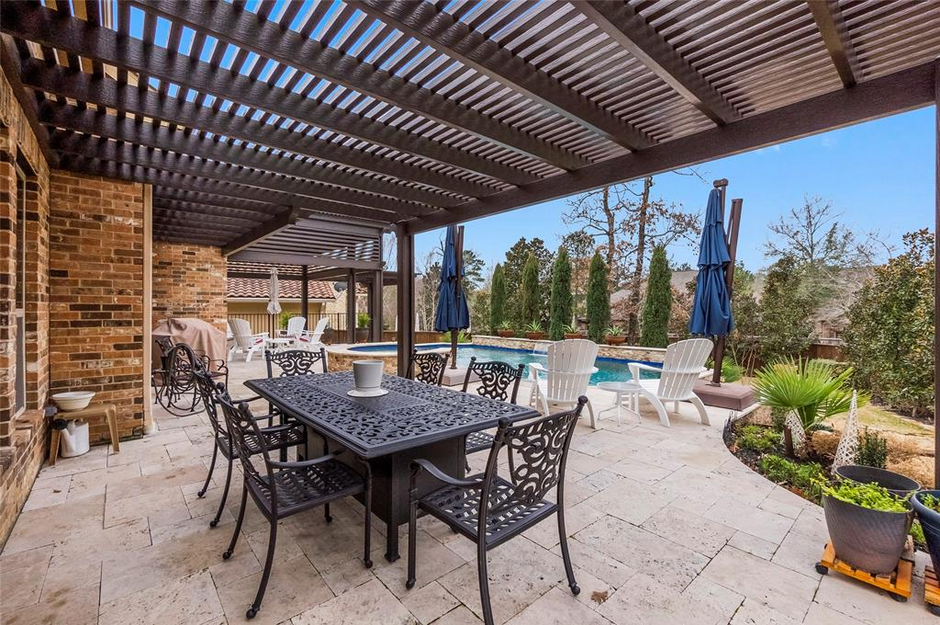A patio with a table and chairs under a pergola next to a pool.
