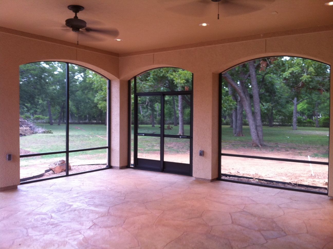 an empty screen patio room with arched windows and a ceiling fan