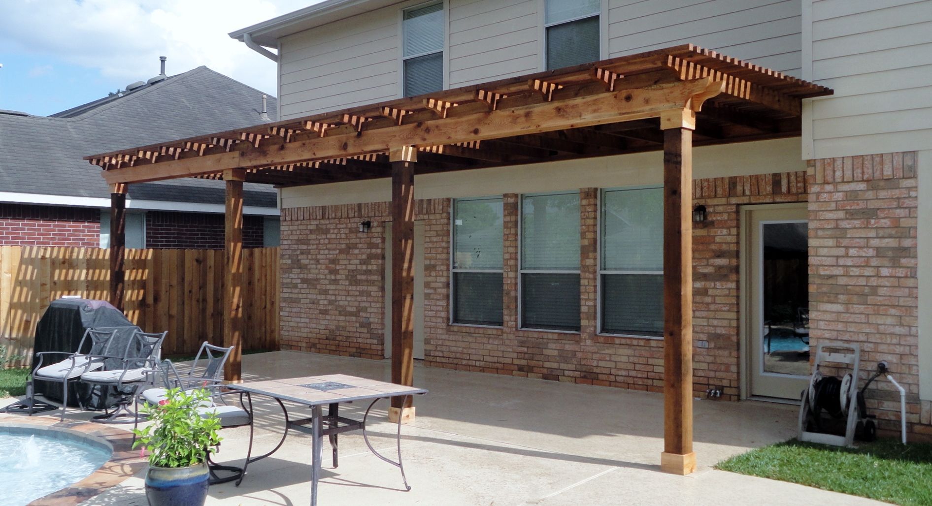 a house with a wooden pergola over a patio with a table and chairs