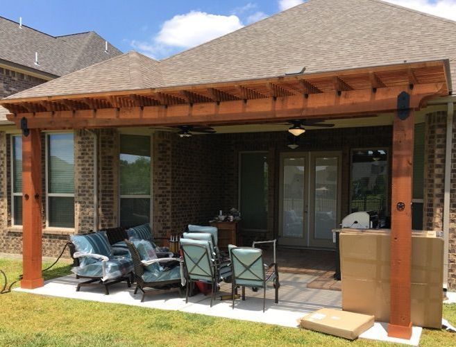 a patio with a cedar pergola and chairs in front of a house .