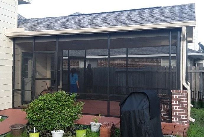 A screened in porch in Houston with a grill and potted plants.