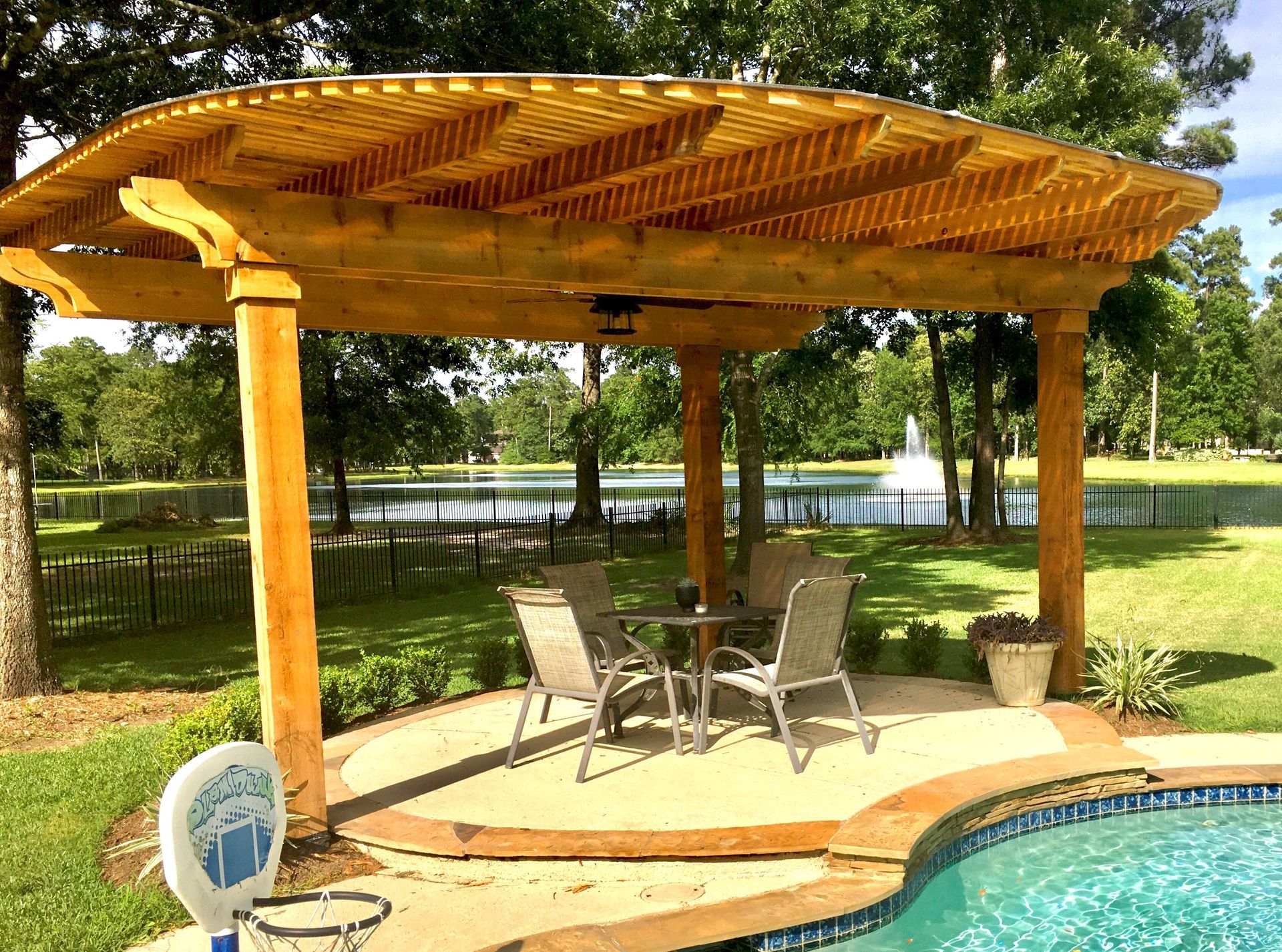 a wooden pergola over a swimming pool with a table and chairs underneath it