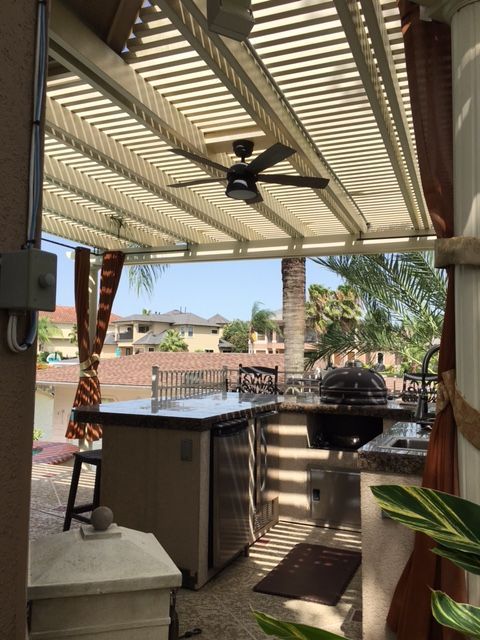 An outdoor kitchen with a ceiling fan and a large island under an Alumawood pergola in Austin, TX.