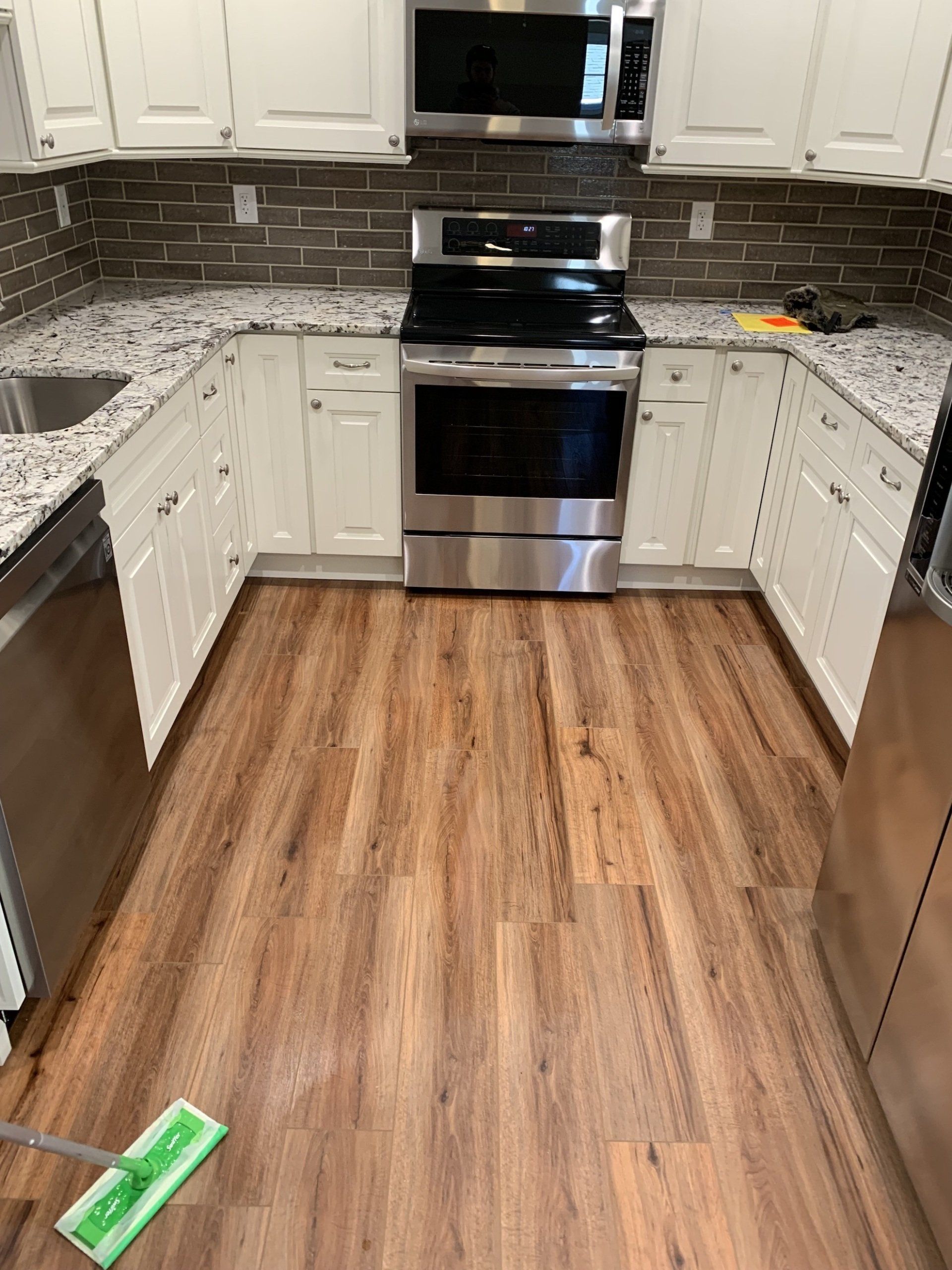 A kitchen with hardwood floors , stainless steel appliances , white cabinets and granite counter tops.