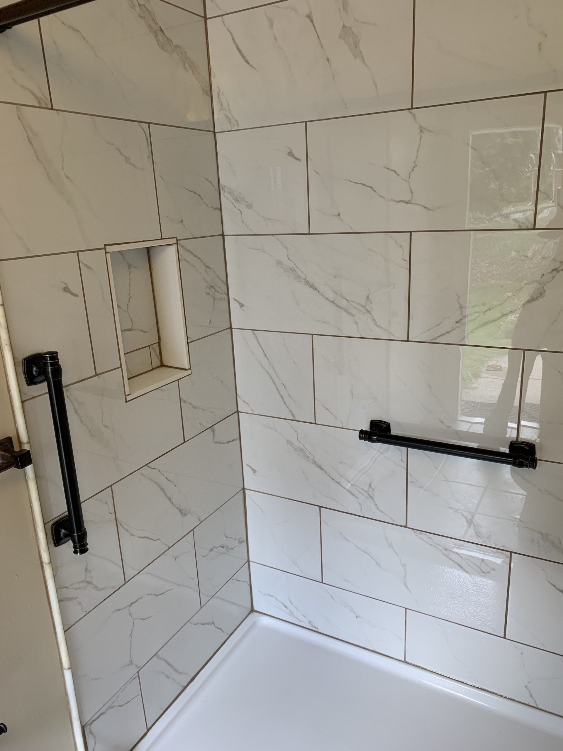 newly remodeled bathroom with tile in shower with hand railset , mirror