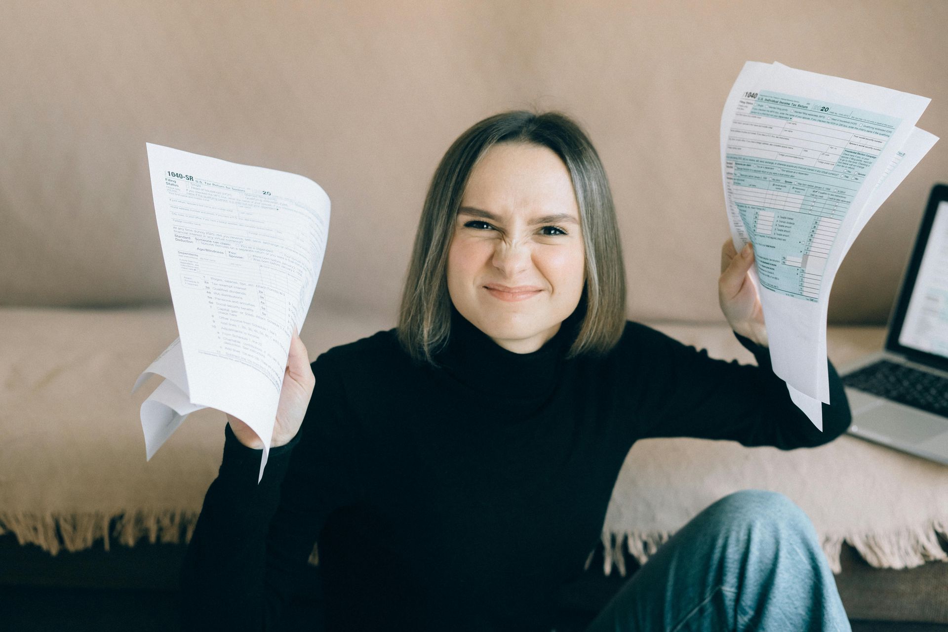 A woman is sitting on the floor holding IRS 1040 tax forms in her hands.