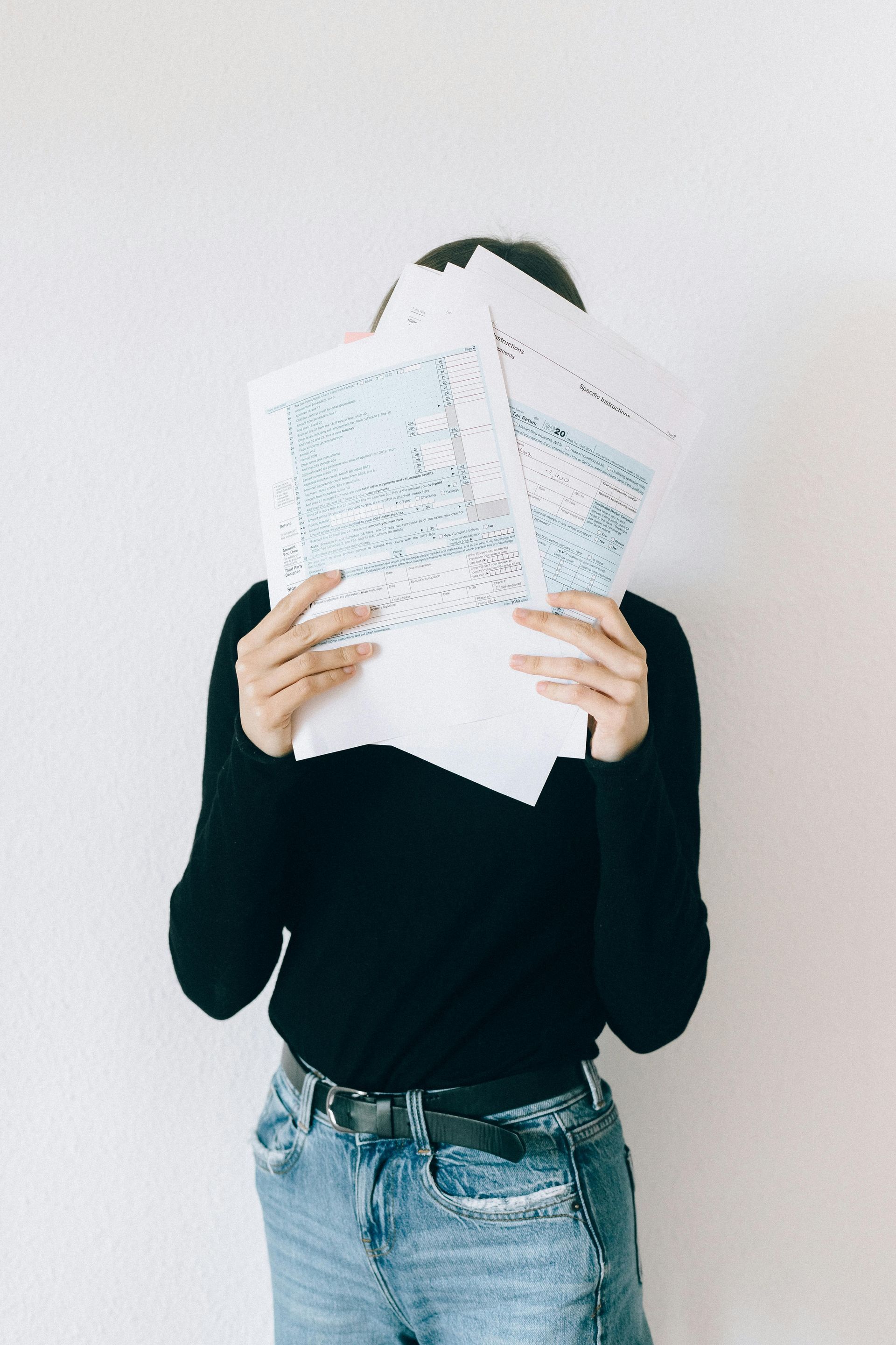 A woman is holding a pieces of paper (tax forms) in front of her face.