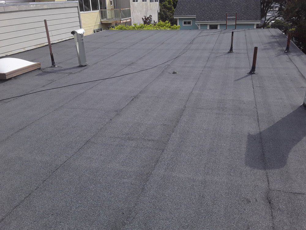 Welder in protective gear working on a metal roof under a bright sky.