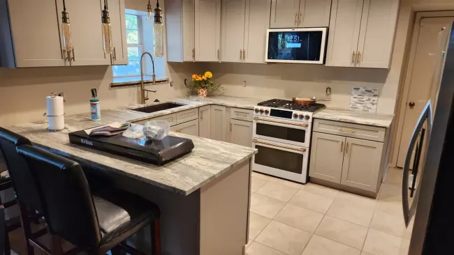 U-shaped kitchen with gray cabinets, granite countertops, and a white oven. Two bar stools are in the foreground.