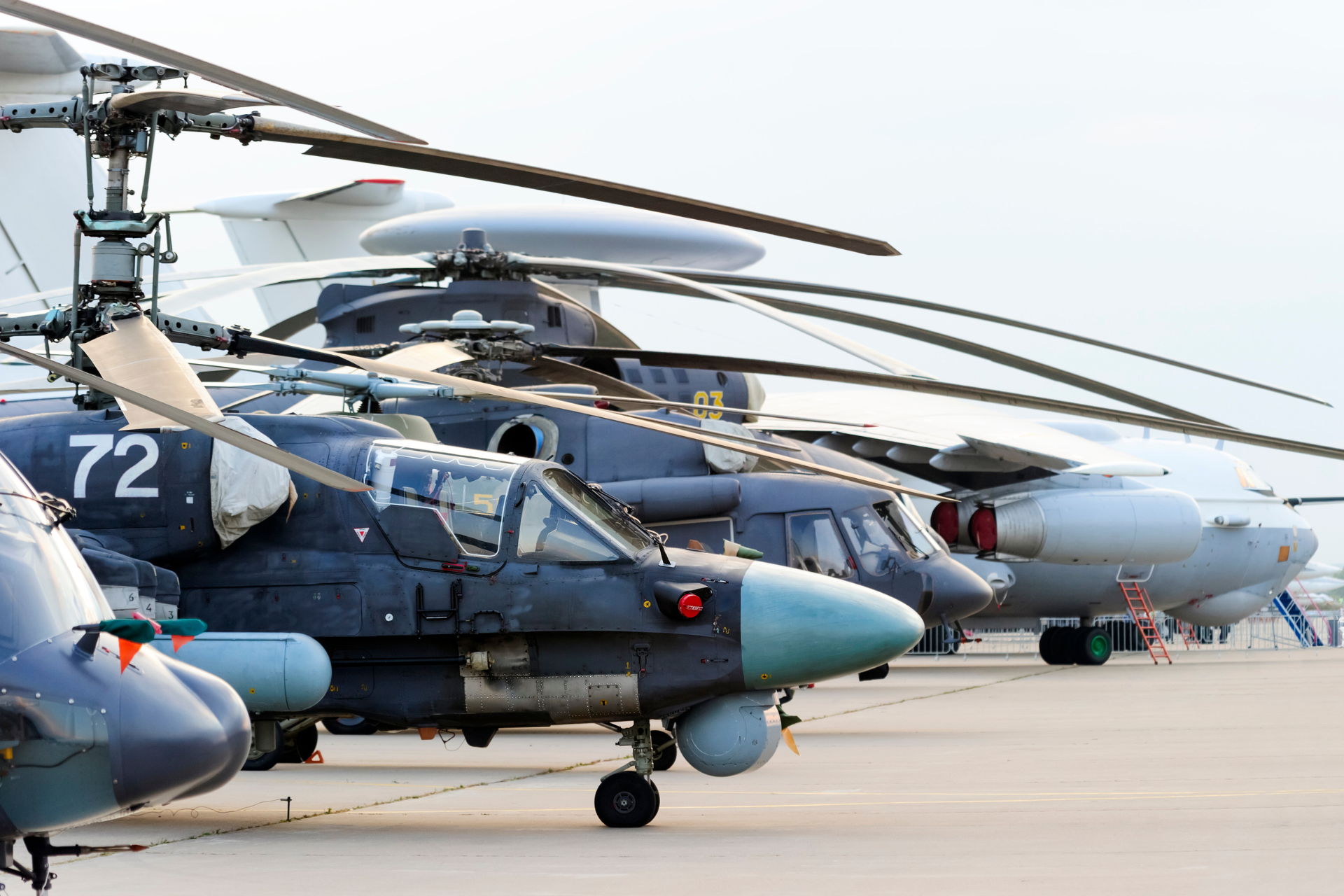 A row of military helicopters are parked on a runway.