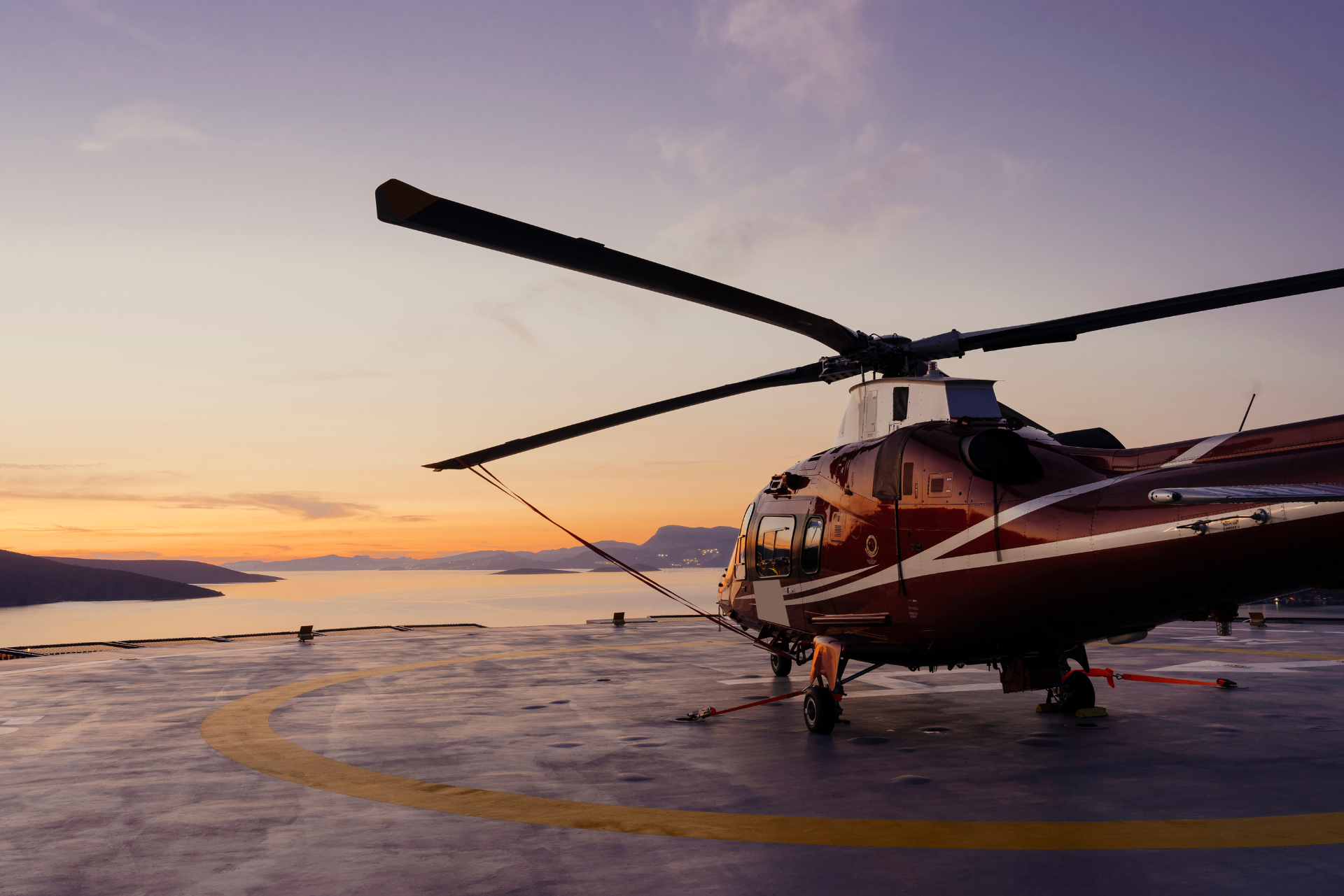 A helicopter is parked on a runway overlooking the ocean at sunset