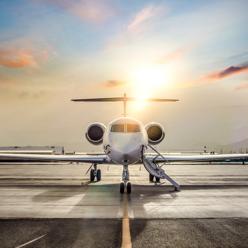 A small private jet is parked on a runway at sunset.