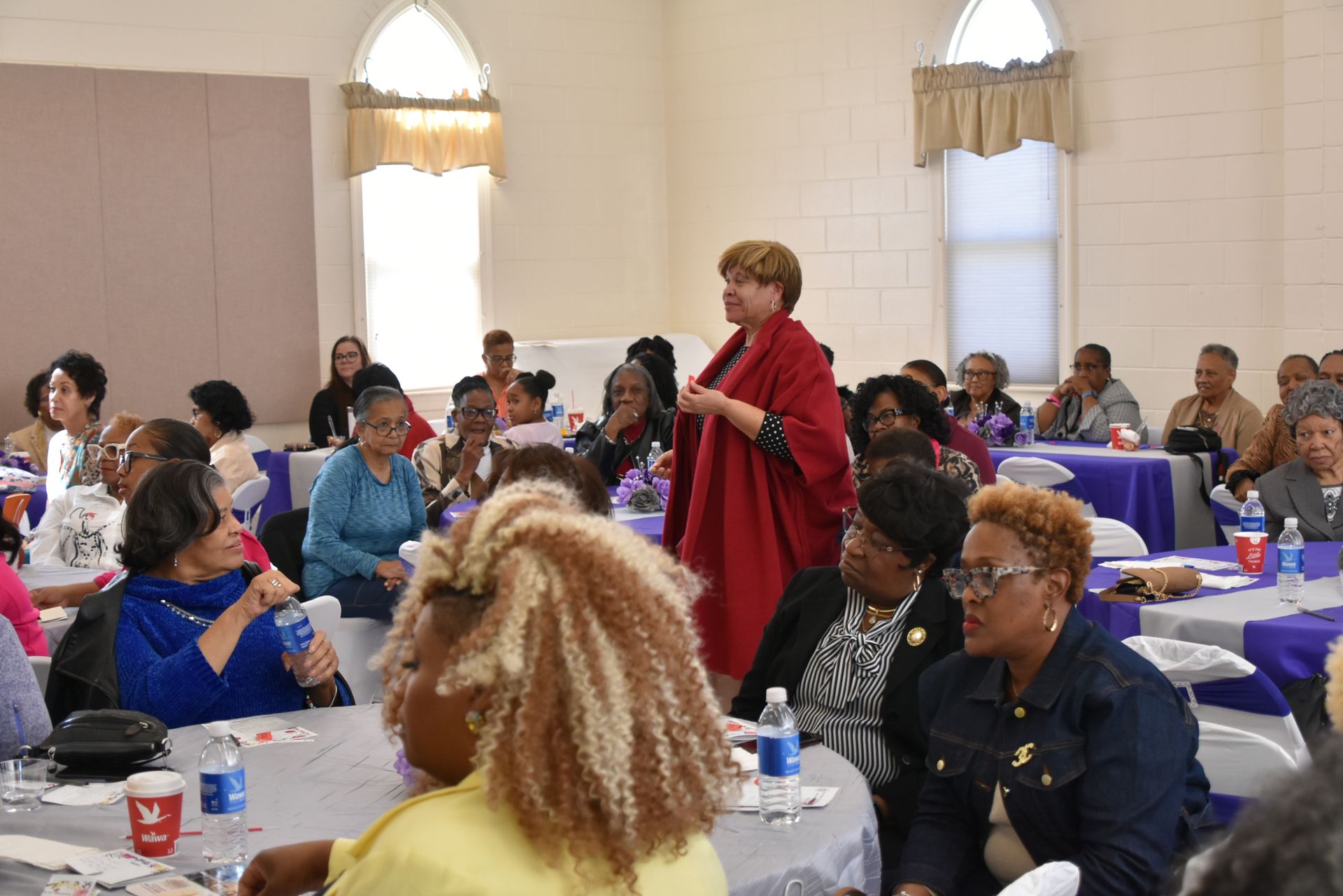 A woman is standing in front of a group of people sitting at tables.