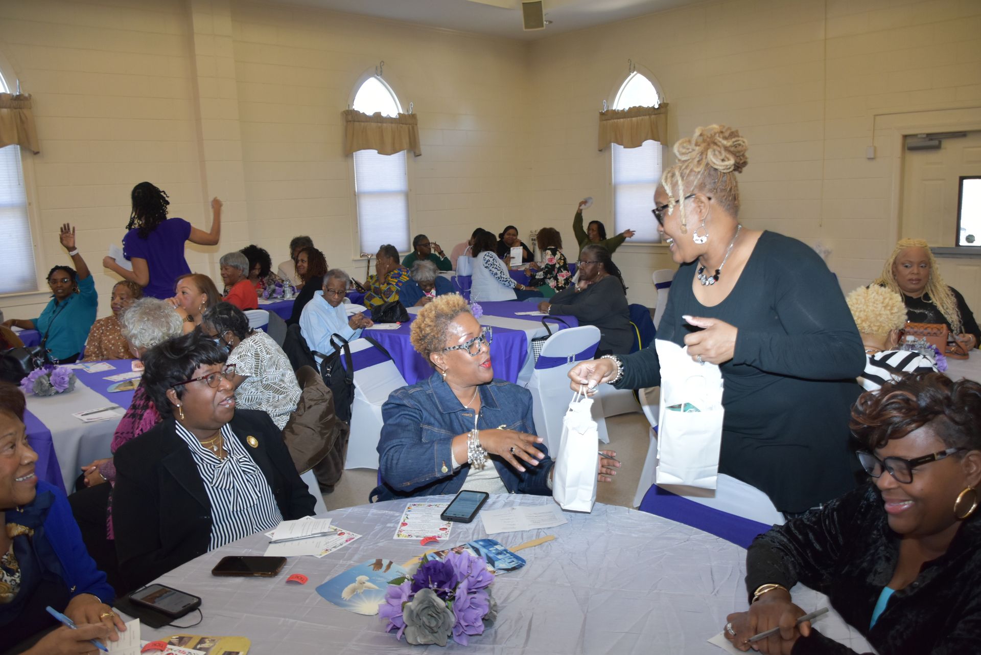A group of women are sitting at tables in a room talking to each other.
