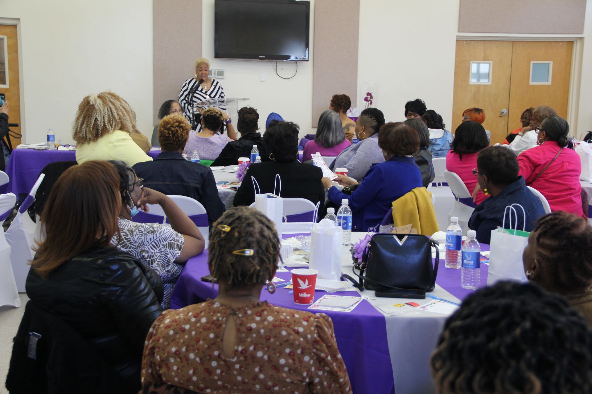 A group of people are sitting at tables in a room watching a presentation
