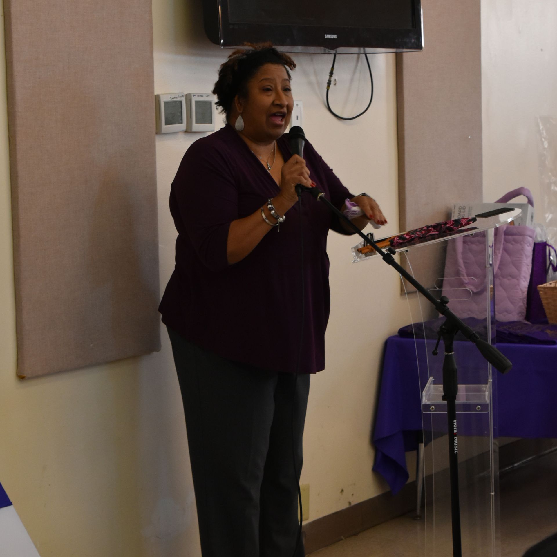 A woman in a purple shirt is speaking into a microphone