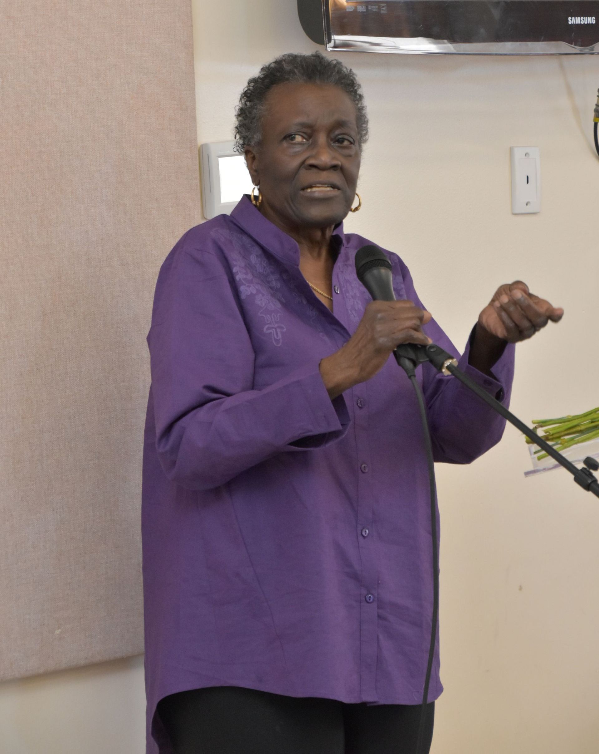 A woman in a purple shirt is speaking into a microphone