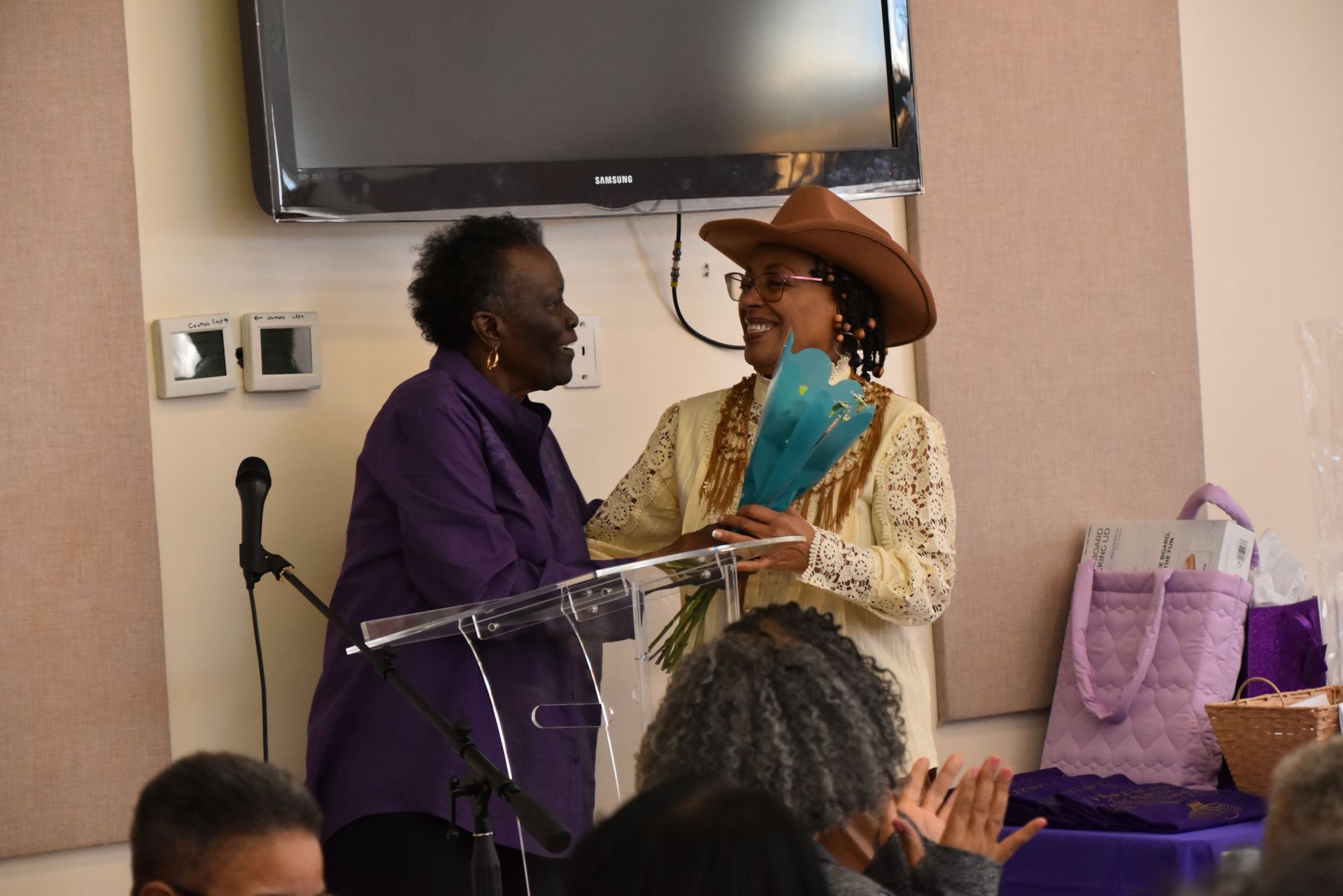 A woman in a cowboy hat is giving a bouquet of flowers to another woman.