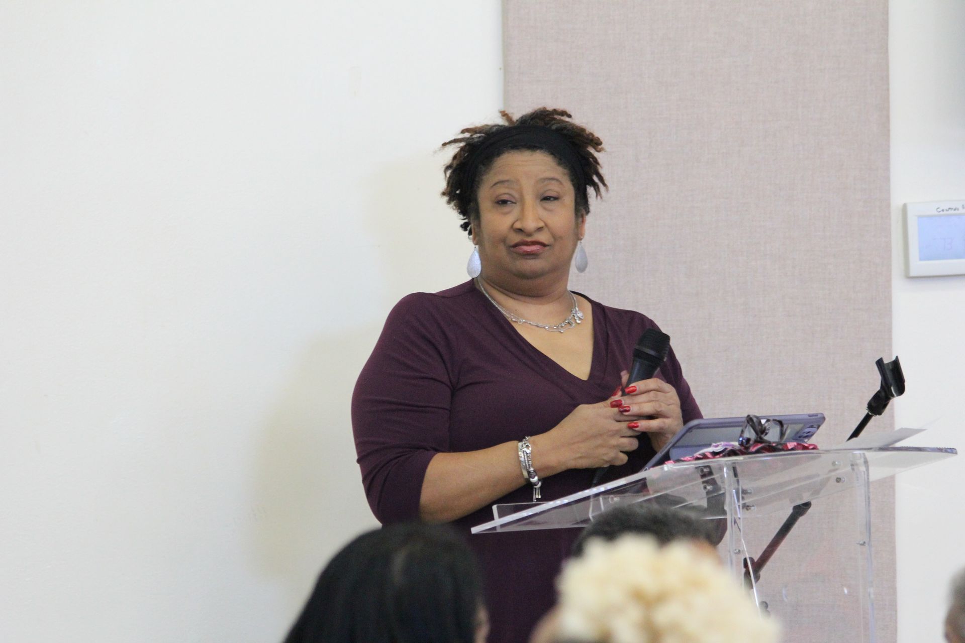 A woman in a purple shirt is standing at a podium holding a microphone.
