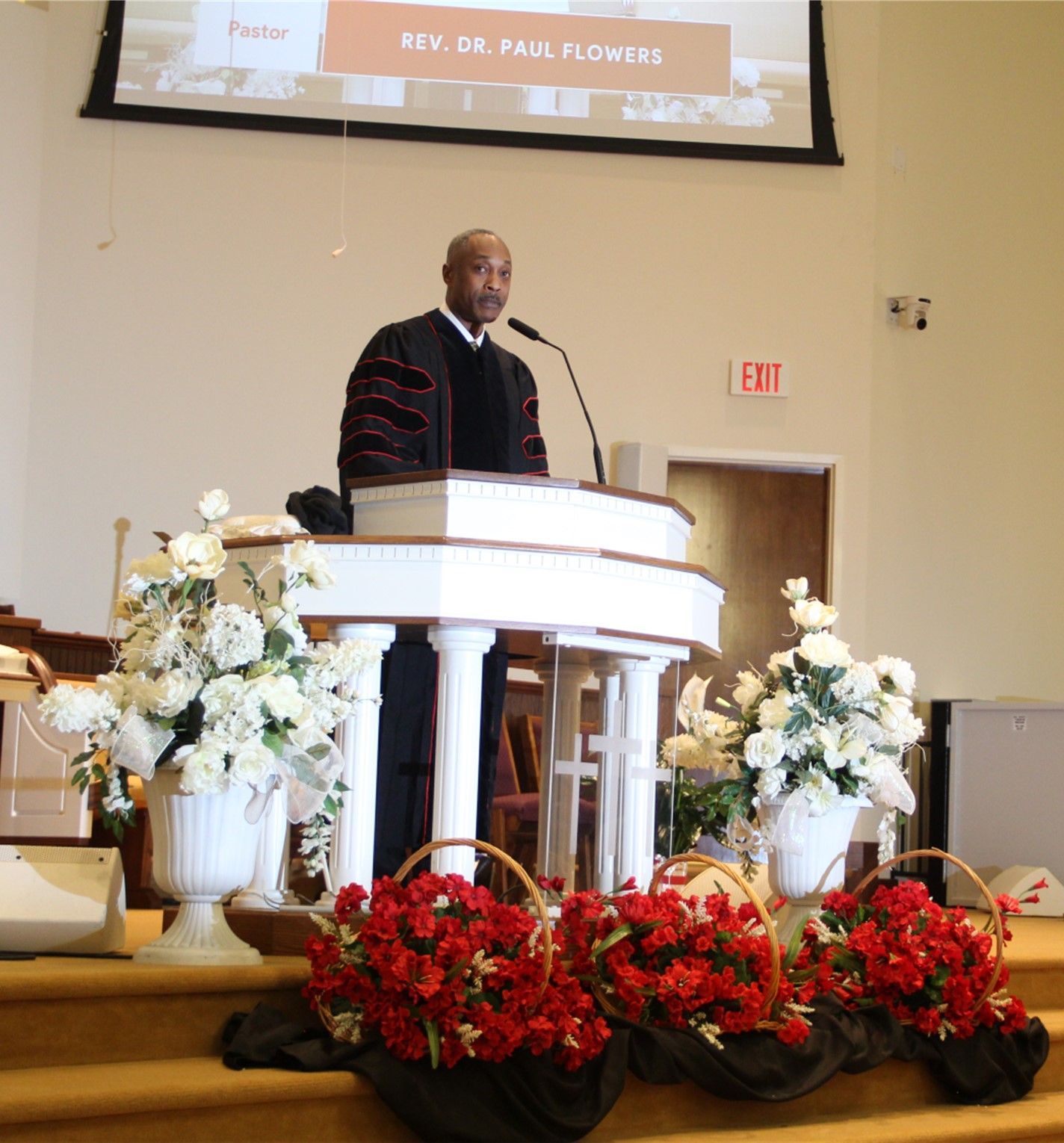 Pastor Paul D. Flowers Sr. stands at a podium with flowers in front of him