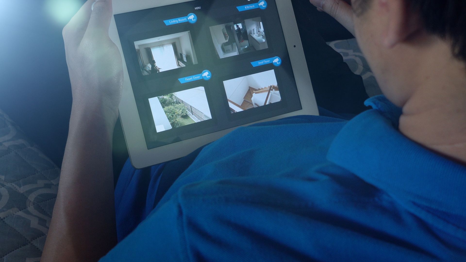 A person holding a tablet, viewing live security camera feeds from inside and outside a building.