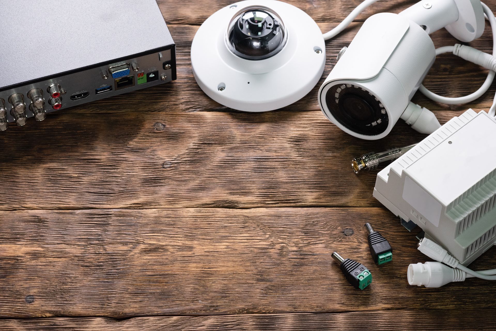 Security camera equipment on a wooden surface. Includes cameras, a recorder, and connectors.