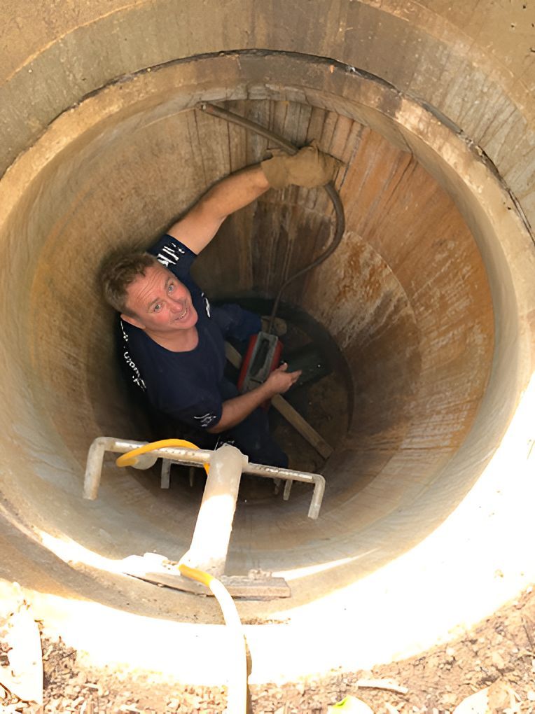 A Man Is Standing In A Manhole With A Ladder — DJ McLean Plumbing in Bonnells Bay, NSW