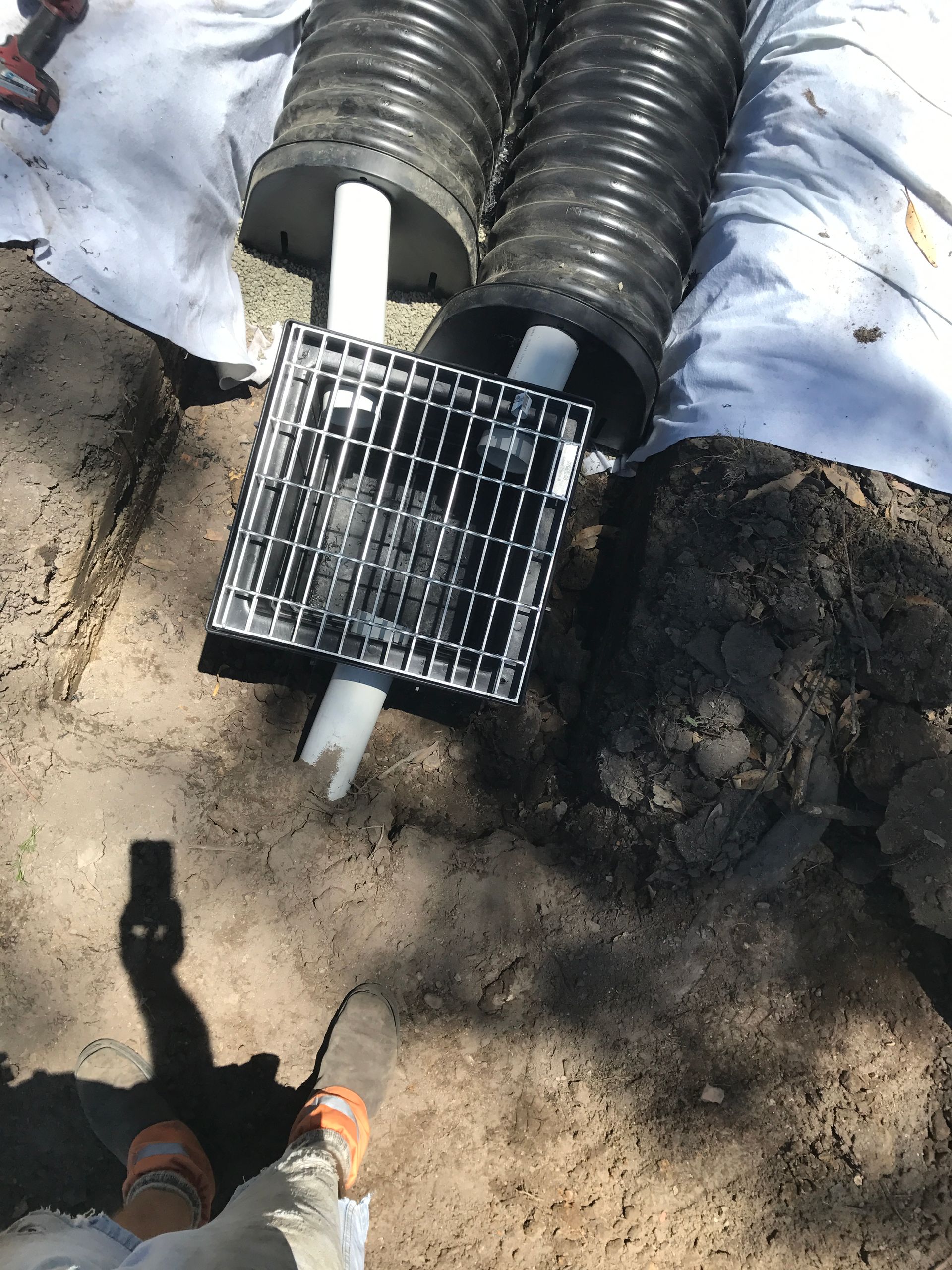 A Person Is Standing Next To A Drain Pipe In The Dirt — DJ McLean Plumbing in Bonnells Bay, NSW