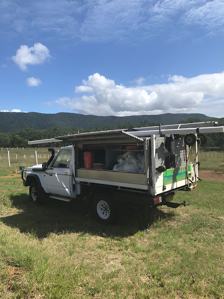 A White Truck With A Canopy Is Parked In A Grassy Field — DJ McLean Plumbing in Bonnells Bay, NSW