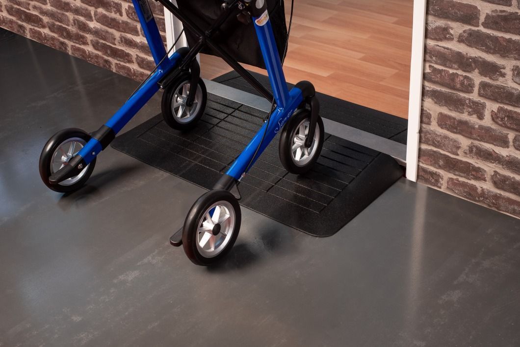 Een blauwe rollator zit op een helling naast een deur.