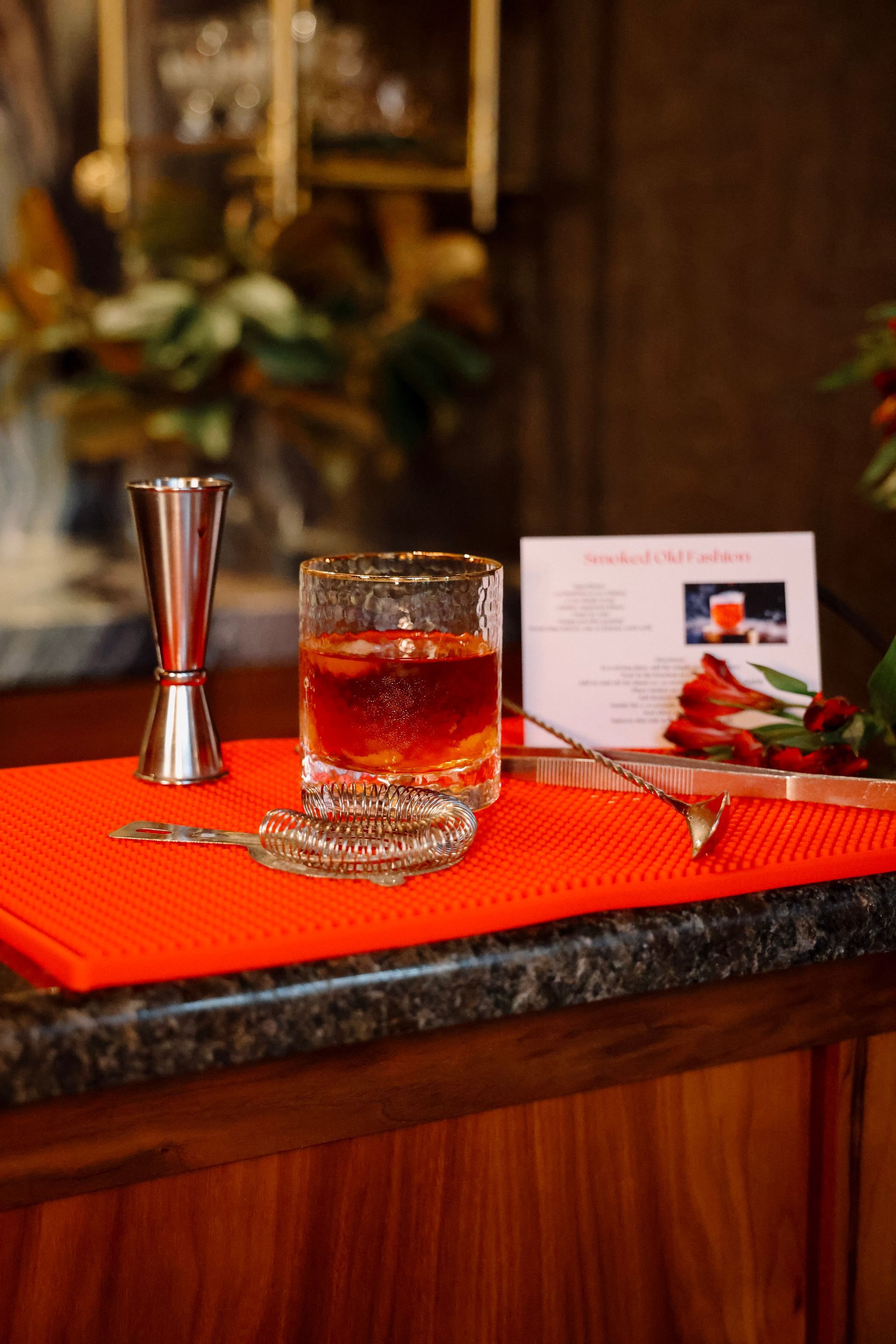 A glass of whiskey is sitting on top of an orange mat on a bar.