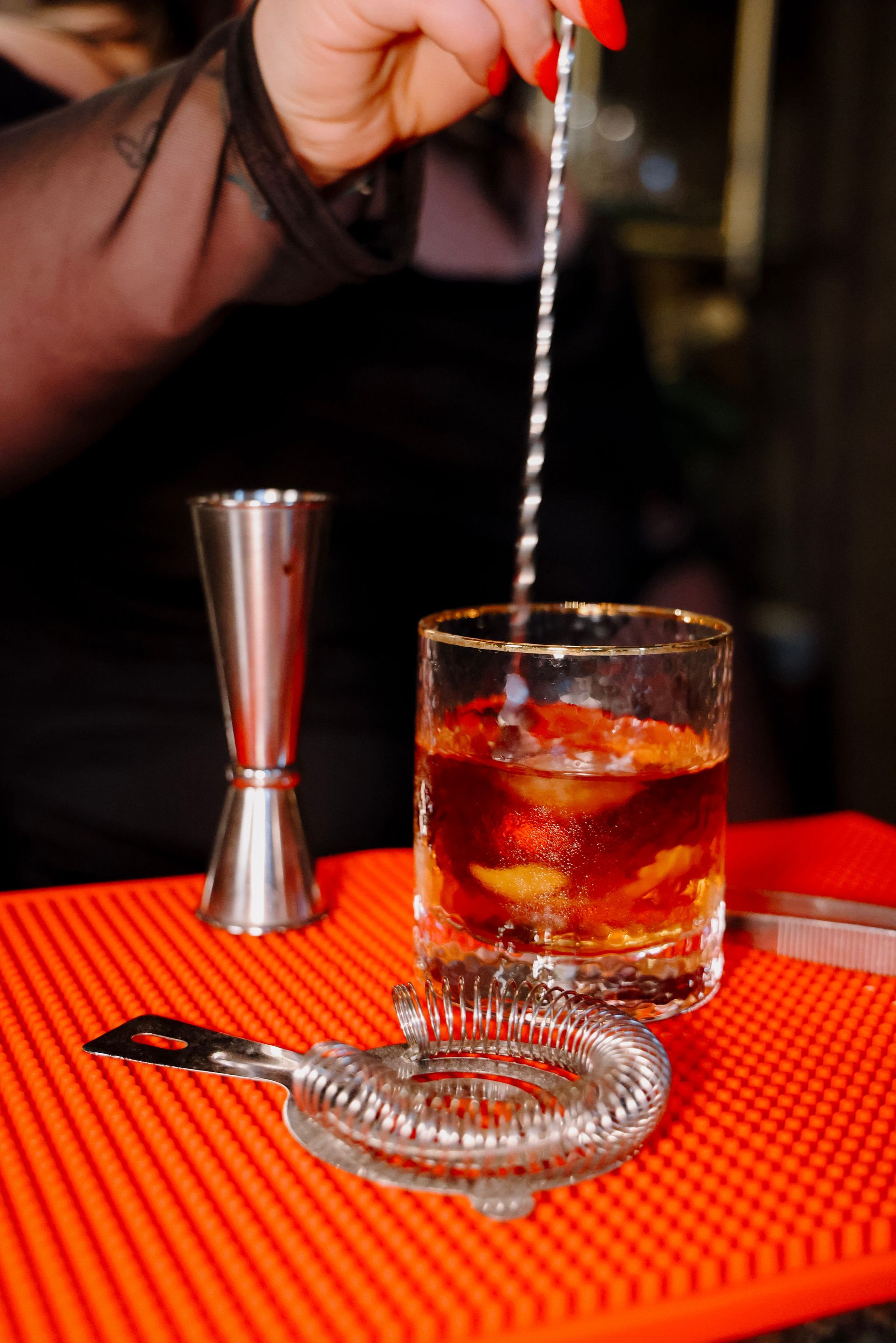 A bartender is stirring a drink in a glass with a straw.